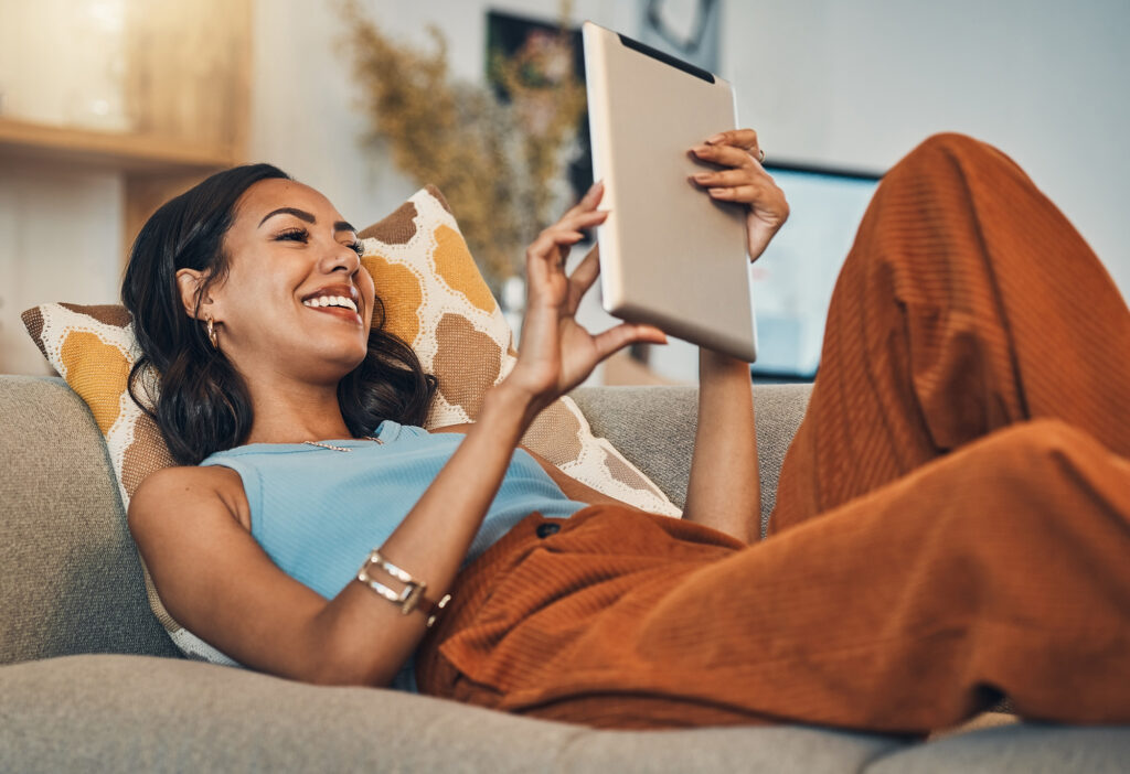 Woman relax on sofa with tablet, online streaming with internet and reading ebook or watching film at home. Happy female person with technology, subscription and mobile app with break in living room.